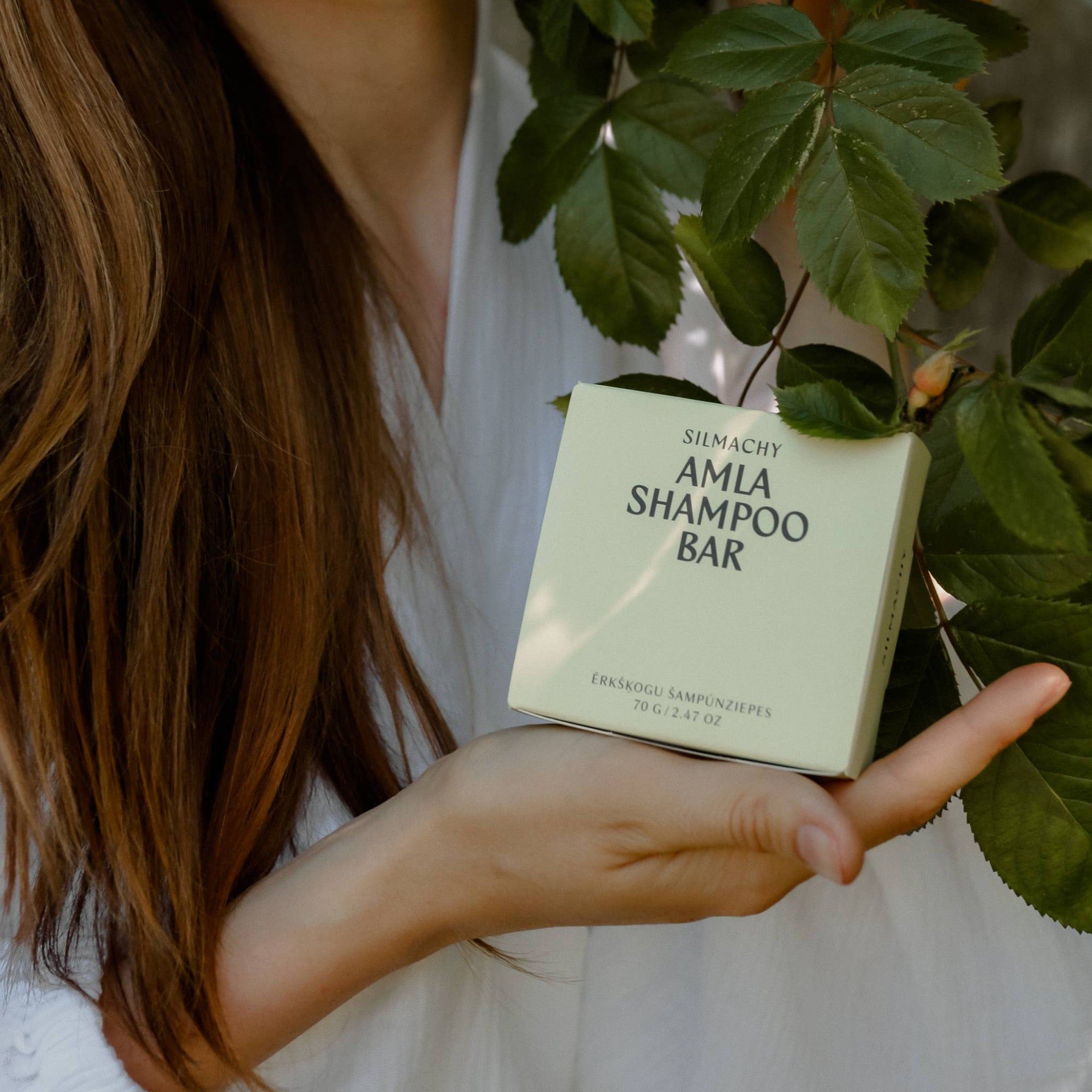 Person holding a Amla Shampoo Bar with green leaves in the background