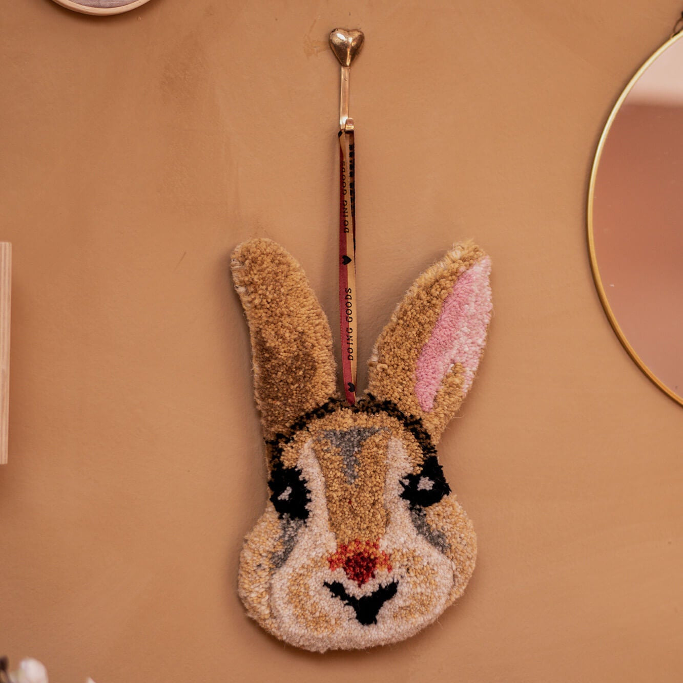 Decorative rabbit-shaped wall hook on a beige wall with a mirror and floral decorations.