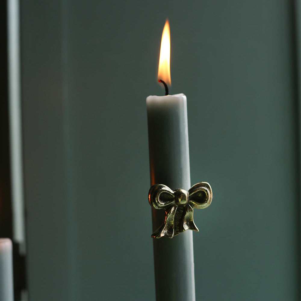 Gray candle with a gold bow holder against a dark background