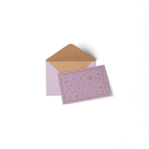 Pink card with gold decorative elements and a matching envelope on a white background