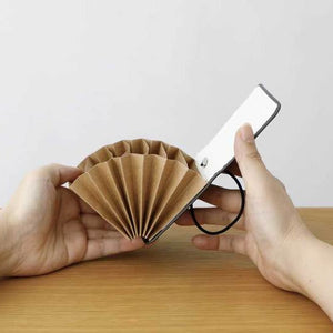 Person holding a small, portable fan and a smartphone on a wooden surface with a light gray background