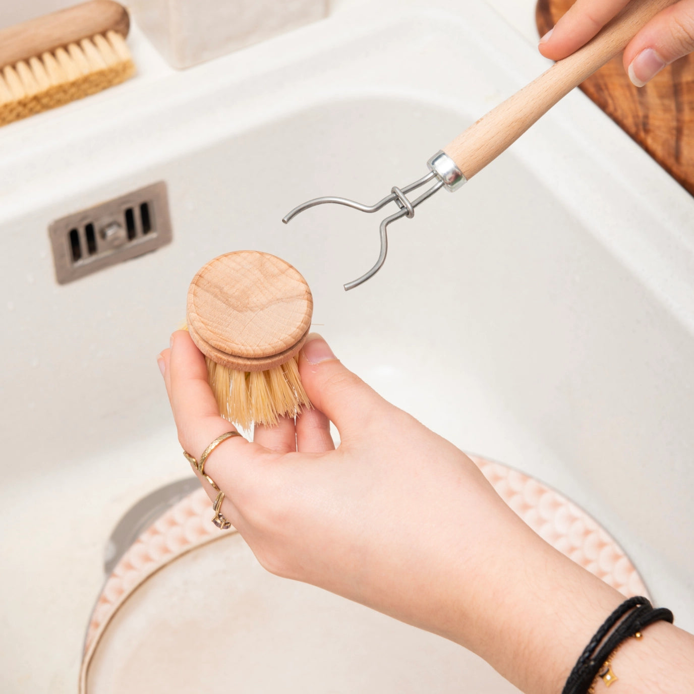 Person holding a wooden dish brush and a metal scrubber over a sink.