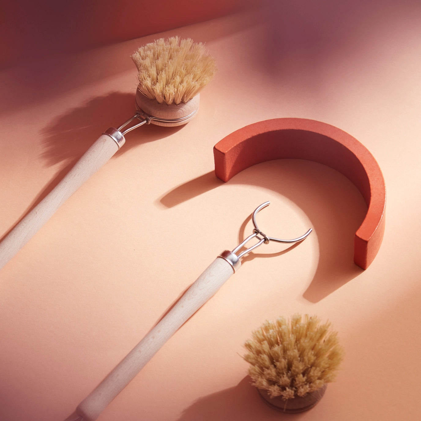Two scrub brushes with natural bristles on a peach-colored surface.