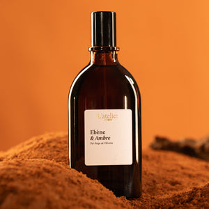 Bottle of L'Atelier Ebene & Ambre perfume on a textured orange surface with an orange background
