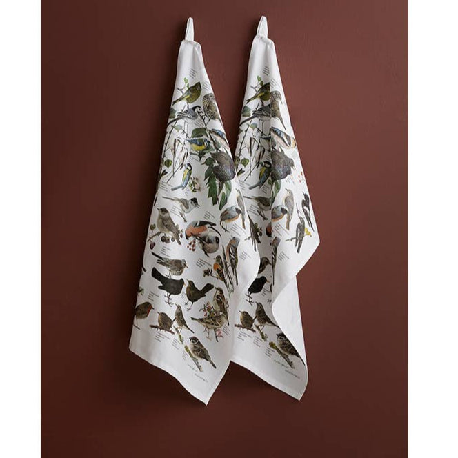 Two white towels with bird prints hanging against a brown wall.