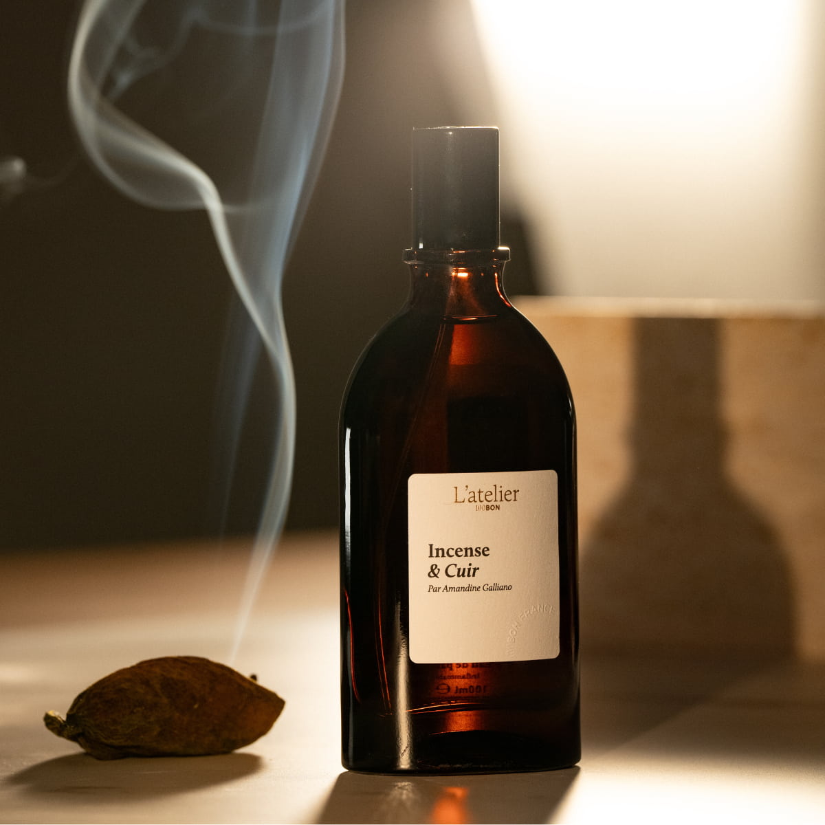 Bottle of L'atelier du Parfum with incense stick and smoke on a wooden surface