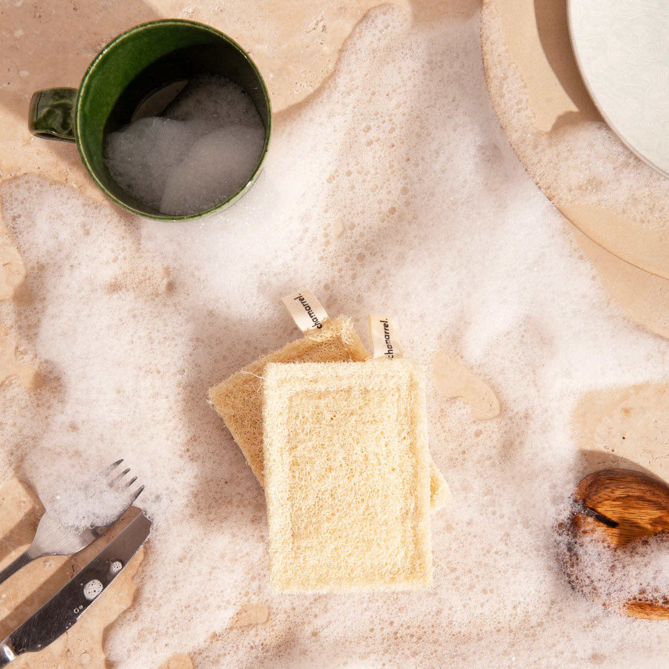 Suds covering a surface with a green mug, fork, knife, and wooden spoon.