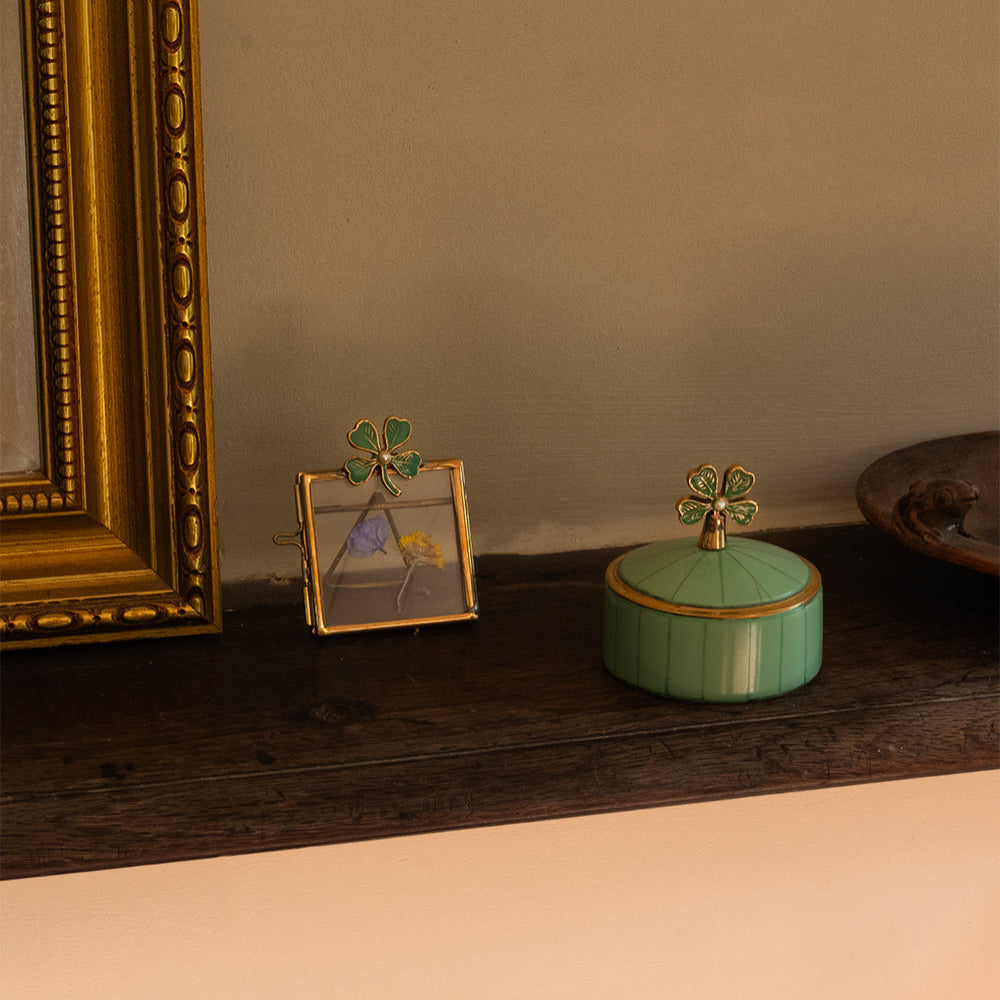 Decorative items including a gold-framed picture and a green container with a gold lid on a wooden surface.