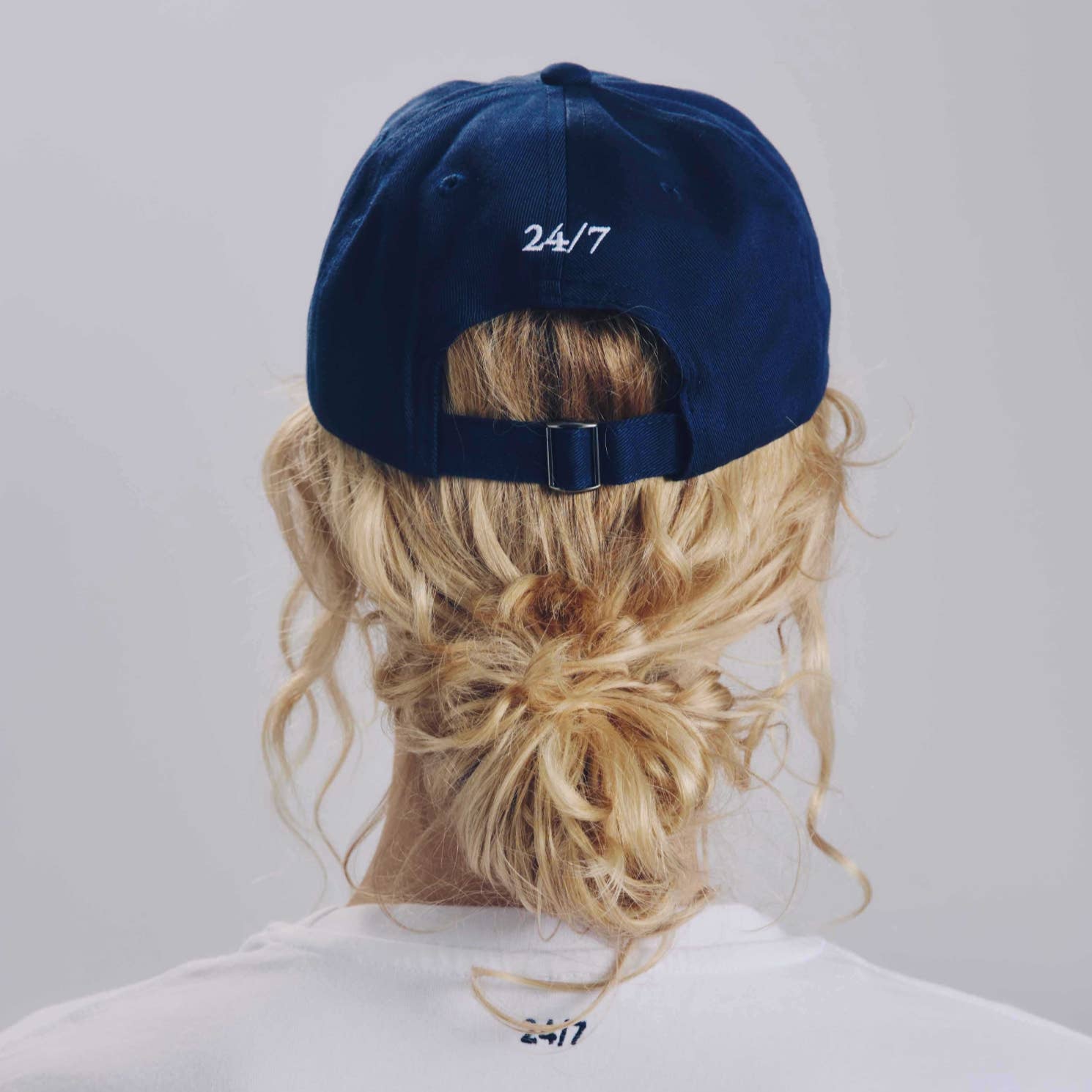 Person wearing a navy blue cap with '24/7' text on a plain background