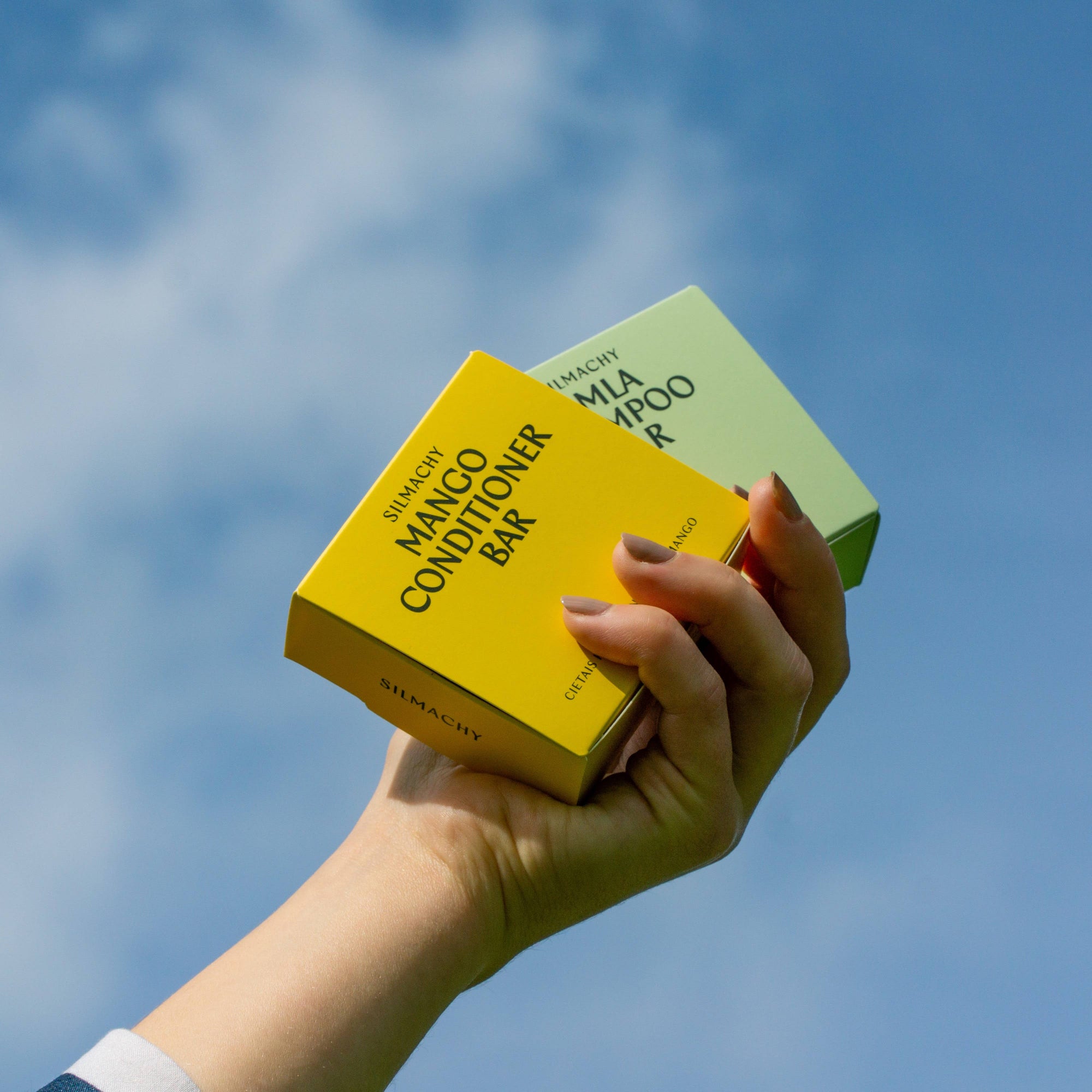 Hand holding two skincare product boxes against a blue sky