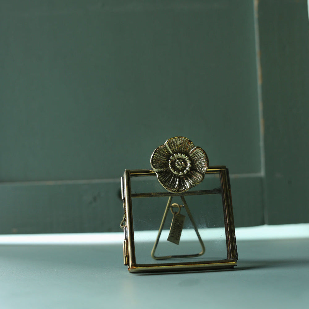 Decorative brass flower-shaped object on a light surface with a green background
