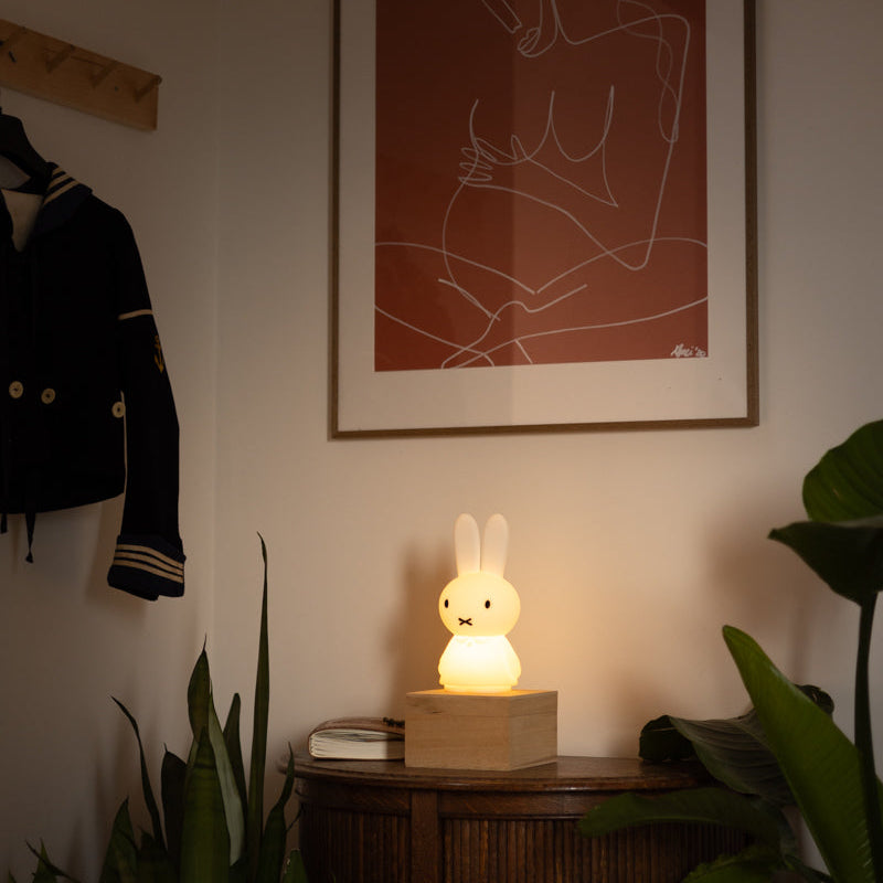 Framed abstract art on a wall with a glowing rabbit-shaped night light on a wooden side table.