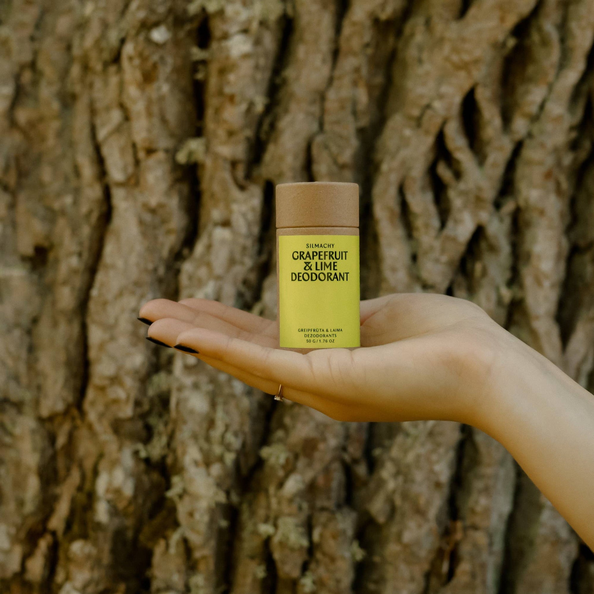 Hand holding a green and brown deodorant container against a tree trunk background