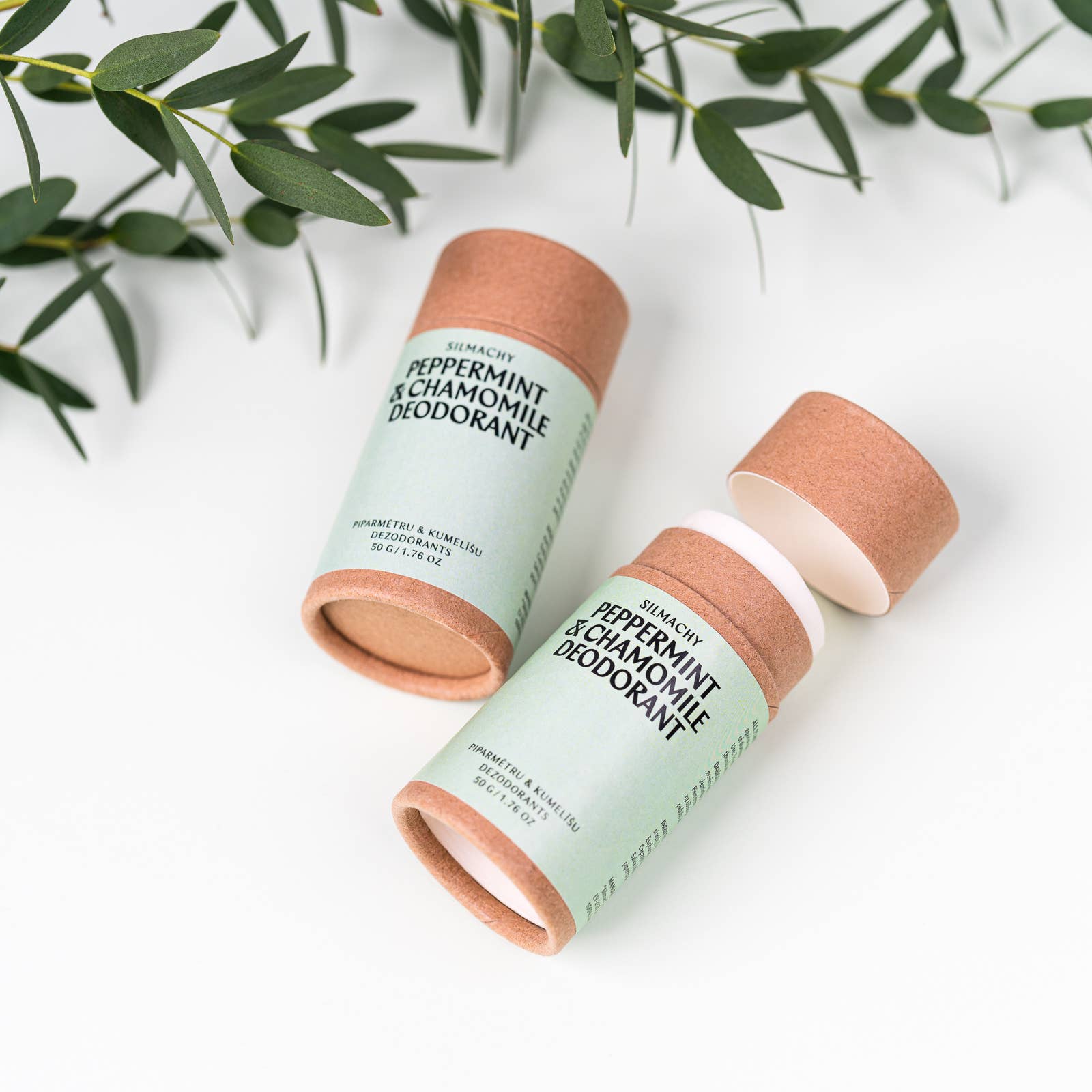 Two deodorant sticks with green labels on a white background with green leaves.