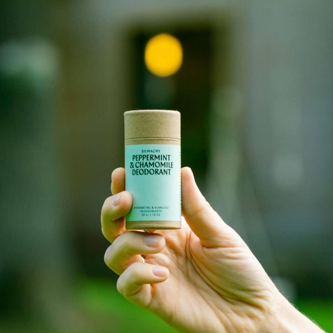 Hand holding a deodorant stick labeled 'Peppermint & Chamomile' against a blurred natural background