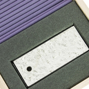 Close-up of a textured rectangular object with a central cutout featuring a small black circle, set against a purple and gray background.