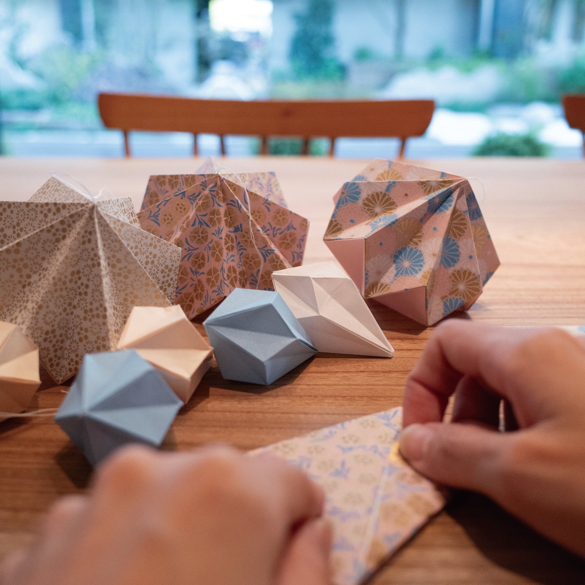 Colorful origami geometric shapes on a wooden table with hands working on another piece.