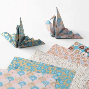 Floral-patterned paper sheets with folded origami cranes on a white background