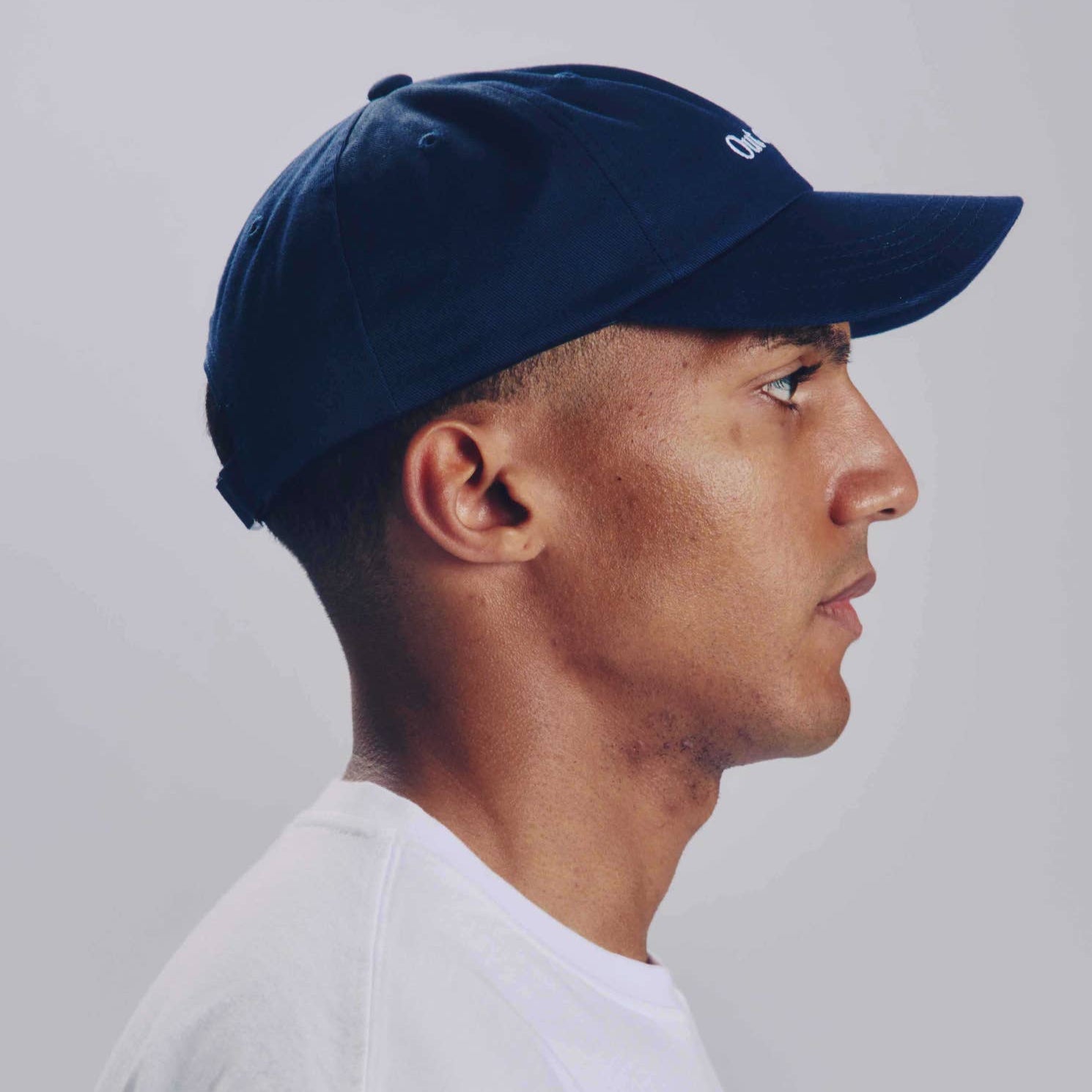 Man wearing a navy blue cap and white shirt against a plain background