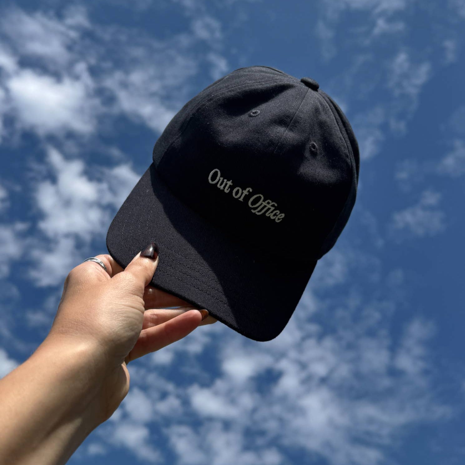 Black cap with 'Out of Office' text held against a blue sky