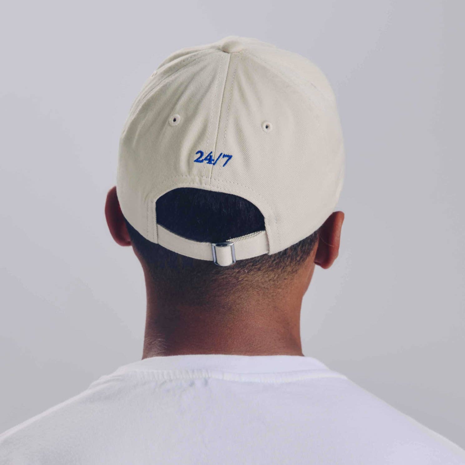 Person wearing a beige cap with '24/7' on the back against a plain background