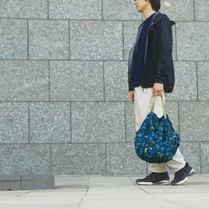Person walking with a blue patterned bag against a gray tiled wall.