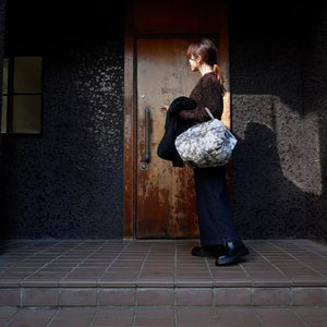 Person holding a floral bag standing in front of a wooden door with a dark, textured wall.