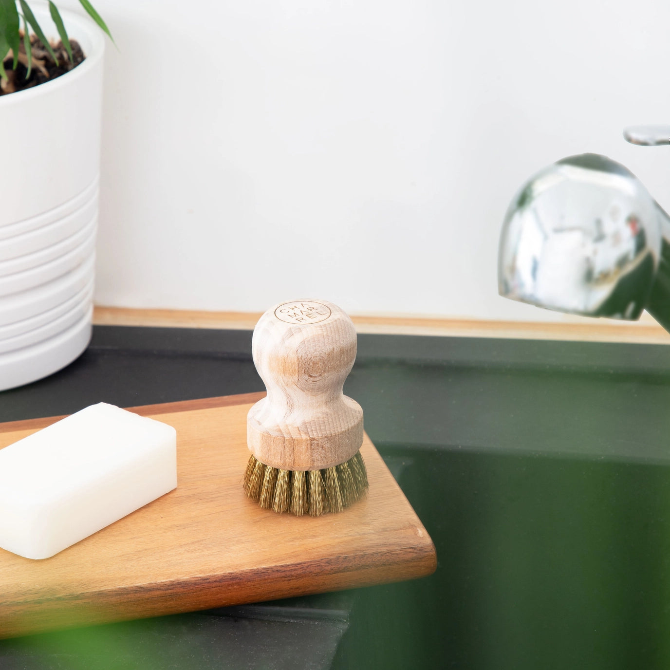 Dish brush on a wooden board with soap next to a green sink.