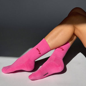 Person wearing bright pink socks with a brand logo on a neutral background