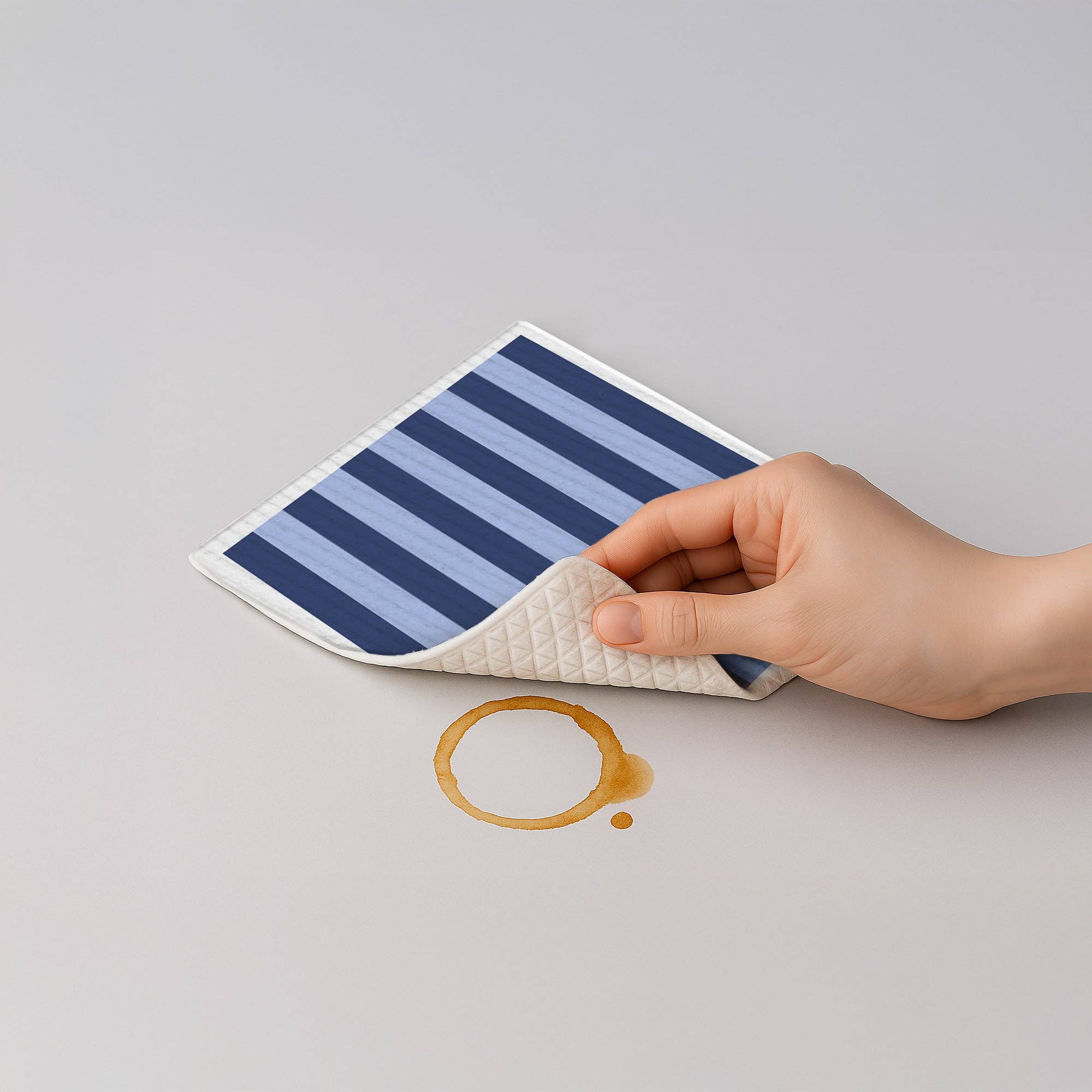 Hand holding a striped mat over a coffee spill on a gray background