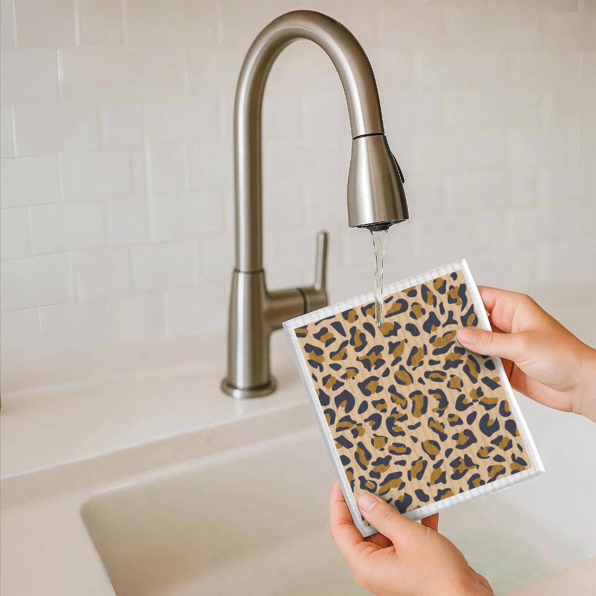 Person holding a leopard print dishcloth under running water from a faucet.