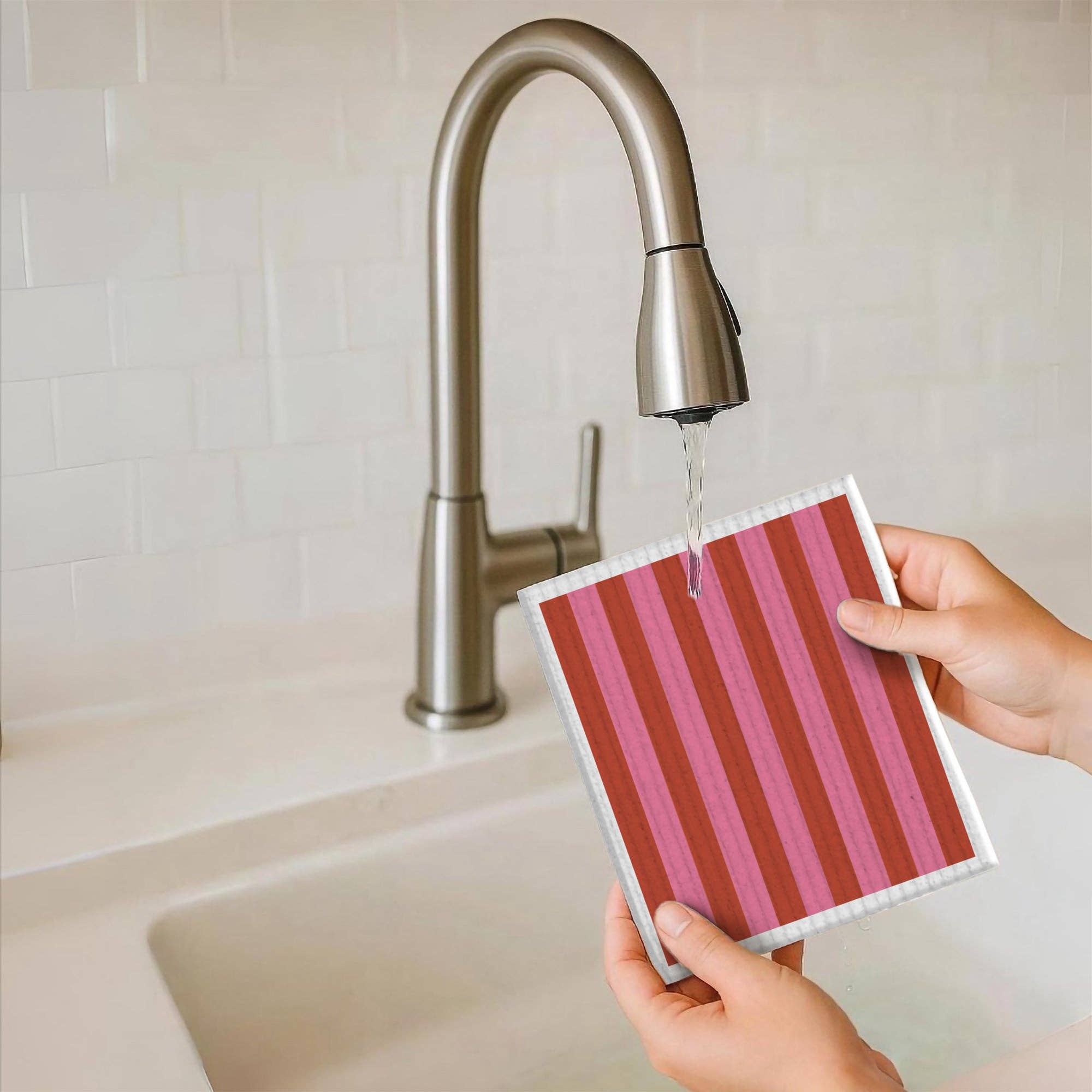 Person holding a striped pink and white cloth under running water from a faucet.