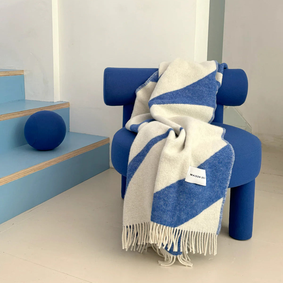 Blue chair with a white and blue patterned throw blanket in a minimalistic room.