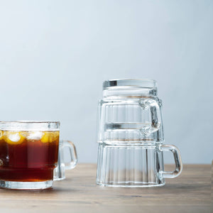 Clear glass mugs with handles on a wooden surface and light blue background