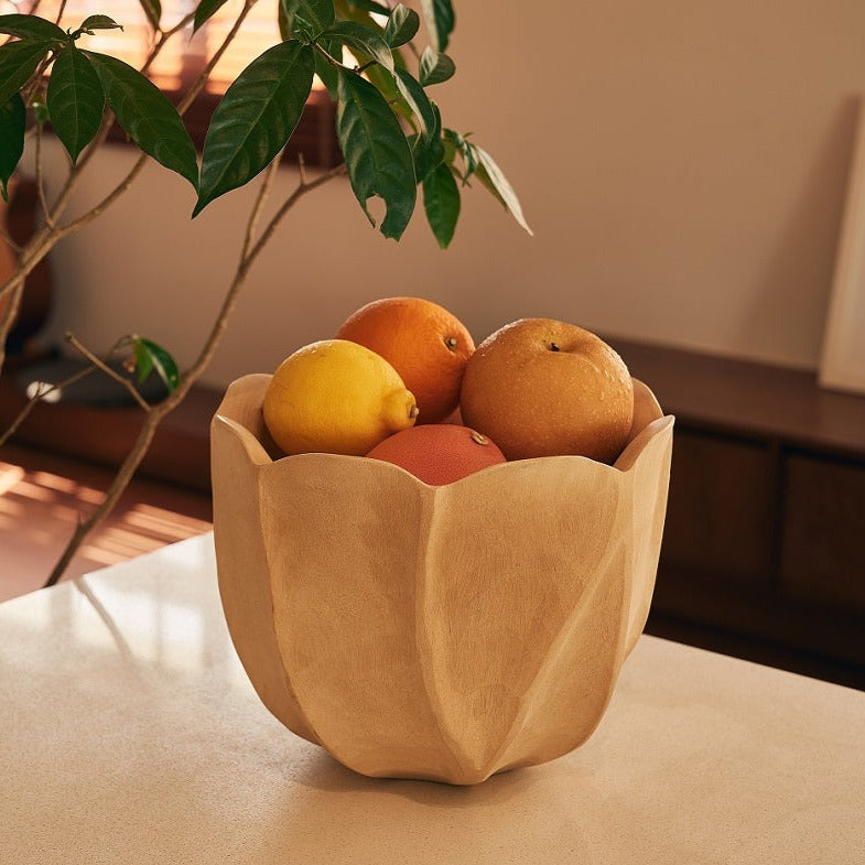 A handcrafted mango wood fruit bowl on a table, filled with various fruits like oranges and apples.