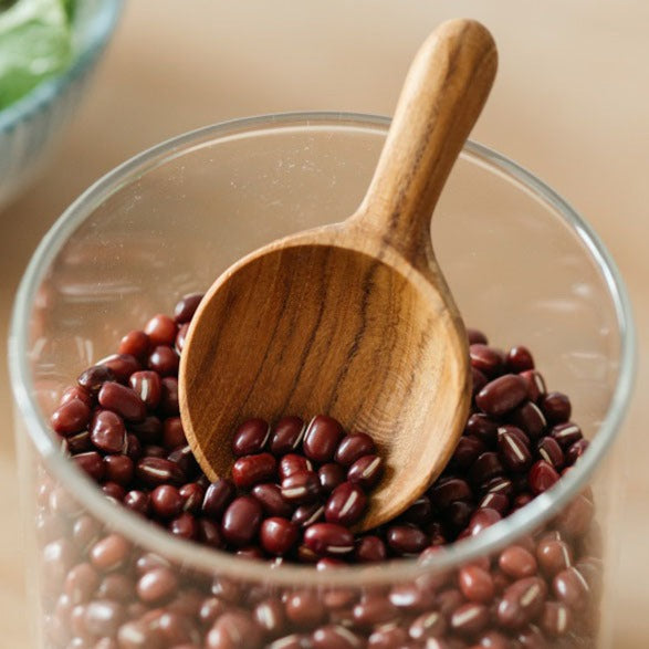 A Teak Wood scoop resting in a glass bowl filled with red kidney beans.