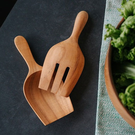 A Teak Wood Salad Serving Set consisting of a spoon and fork, placed on a dark surface next to a bowl of lettuce.