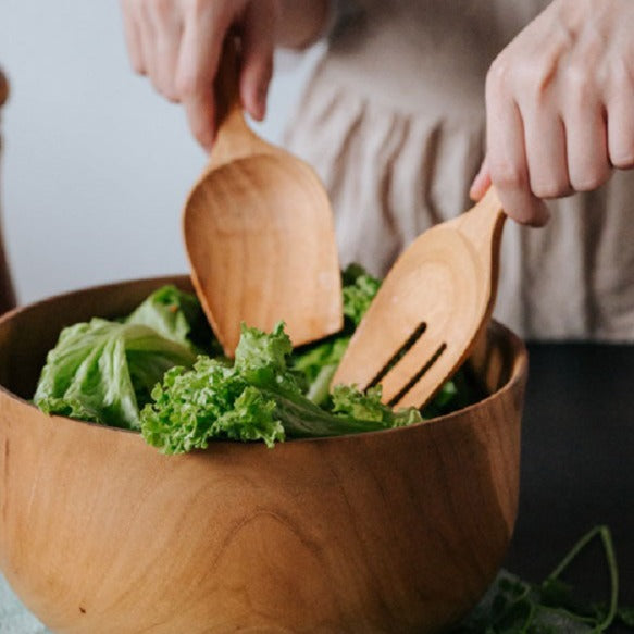 A Teak Wood Salad Serving Set consisting of a spoon and fork, placed on a dark surface next to a bowl of lettuce.