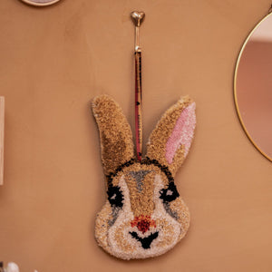 Decorative rabbit-shaped wall hook on a beige wall with a mirror and floral decorations.