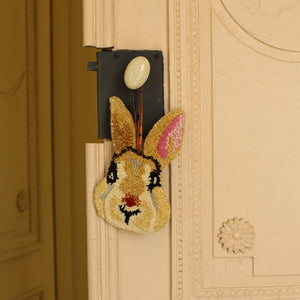 Decorative rabbit-shaped object on a door handle against a beige wall with decorative molding.