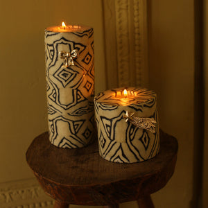 Two patterned candles on a wooden stool with a warm glow.