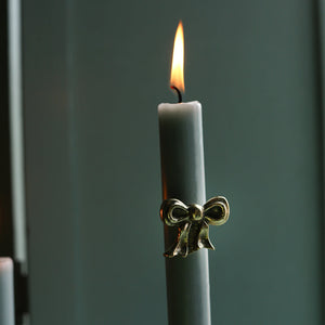 Gray candle with a gold bow holder against a dark background