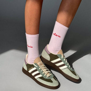 Person wearing green Adidas sneakers with white stripes and pink socks on a gray background