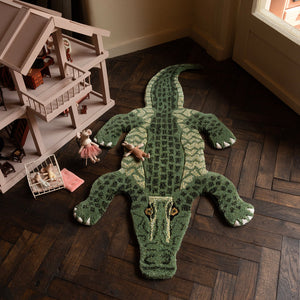 Green alligator rug on a wooden floor with a dollhouse in the background