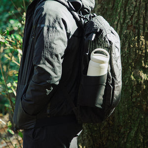 Person wearing a black jacket and backpack with a white water bottle in a forest setting