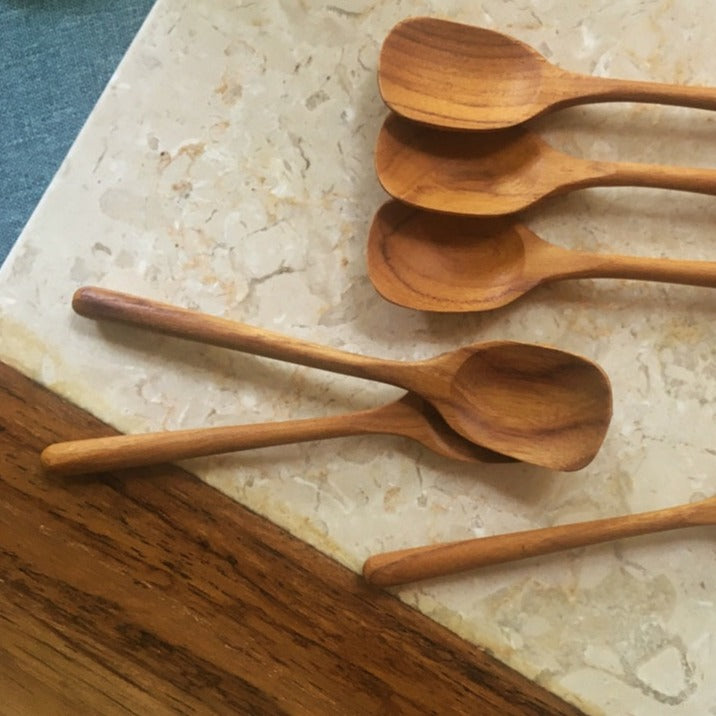 A set of wooden tea spoons with a smooth finish, displayed on a marble surface.