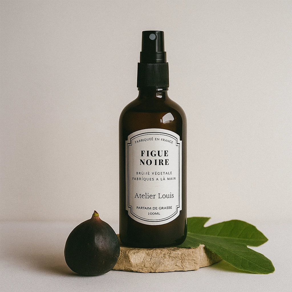 Bottle of 'Figue Noire' with a fig and leaf on a neutral background