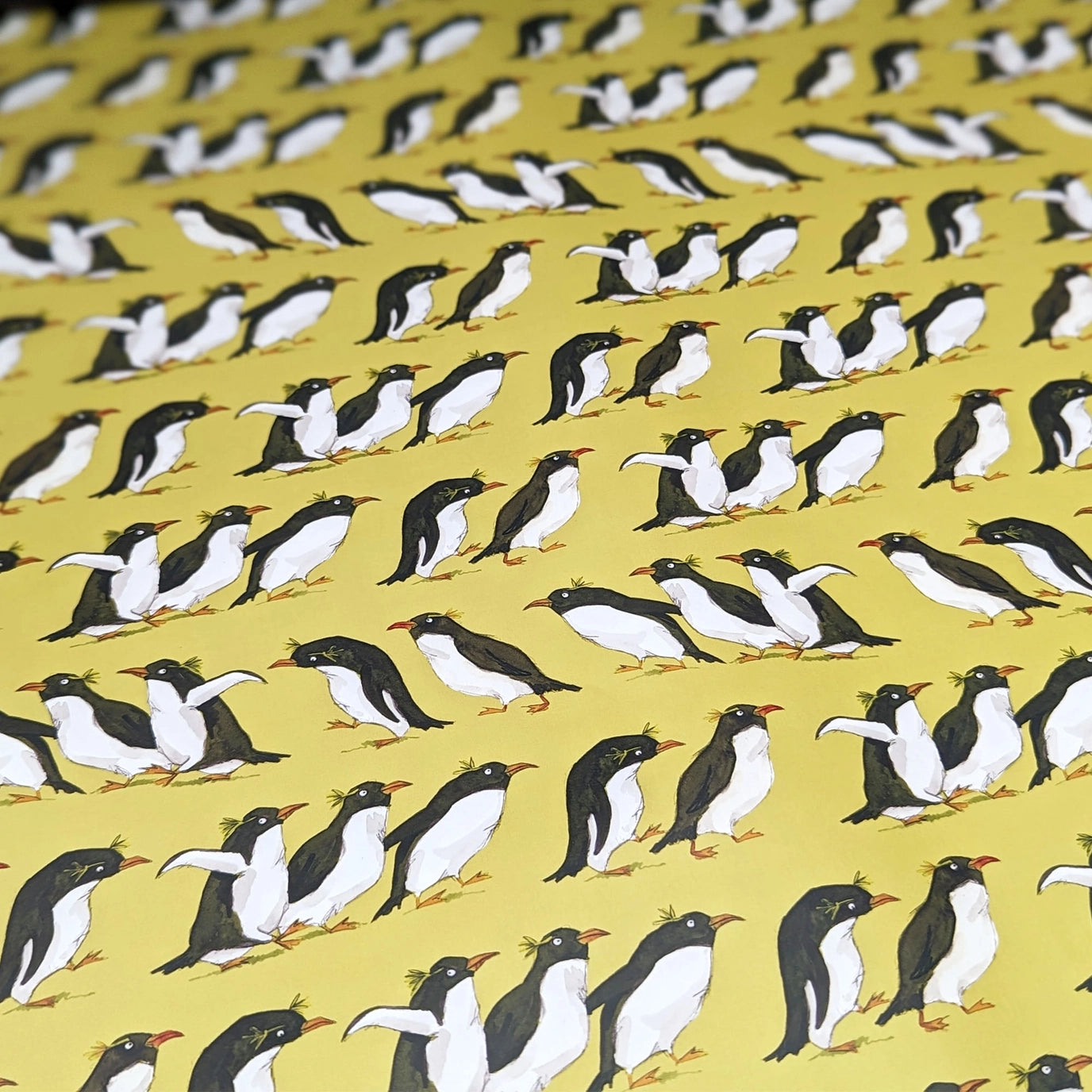 Gift box with penguin pattern and pink ribbon on a matching yellow background