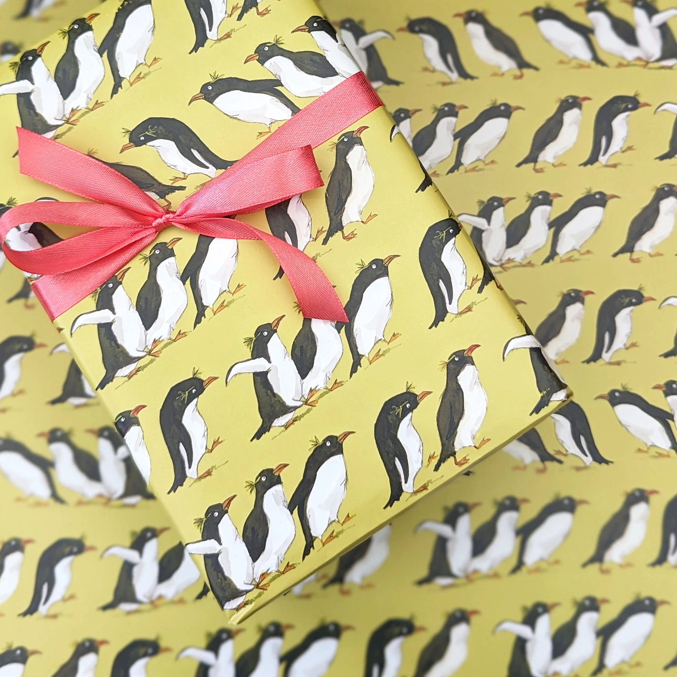 Gift box with penguin pattern and pink ribbon on a matching yellow background