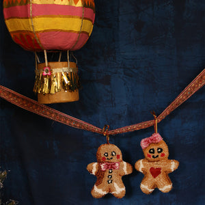 Decorative gingerbread man ornaments hanging from a hot air balloon against a dark blue background